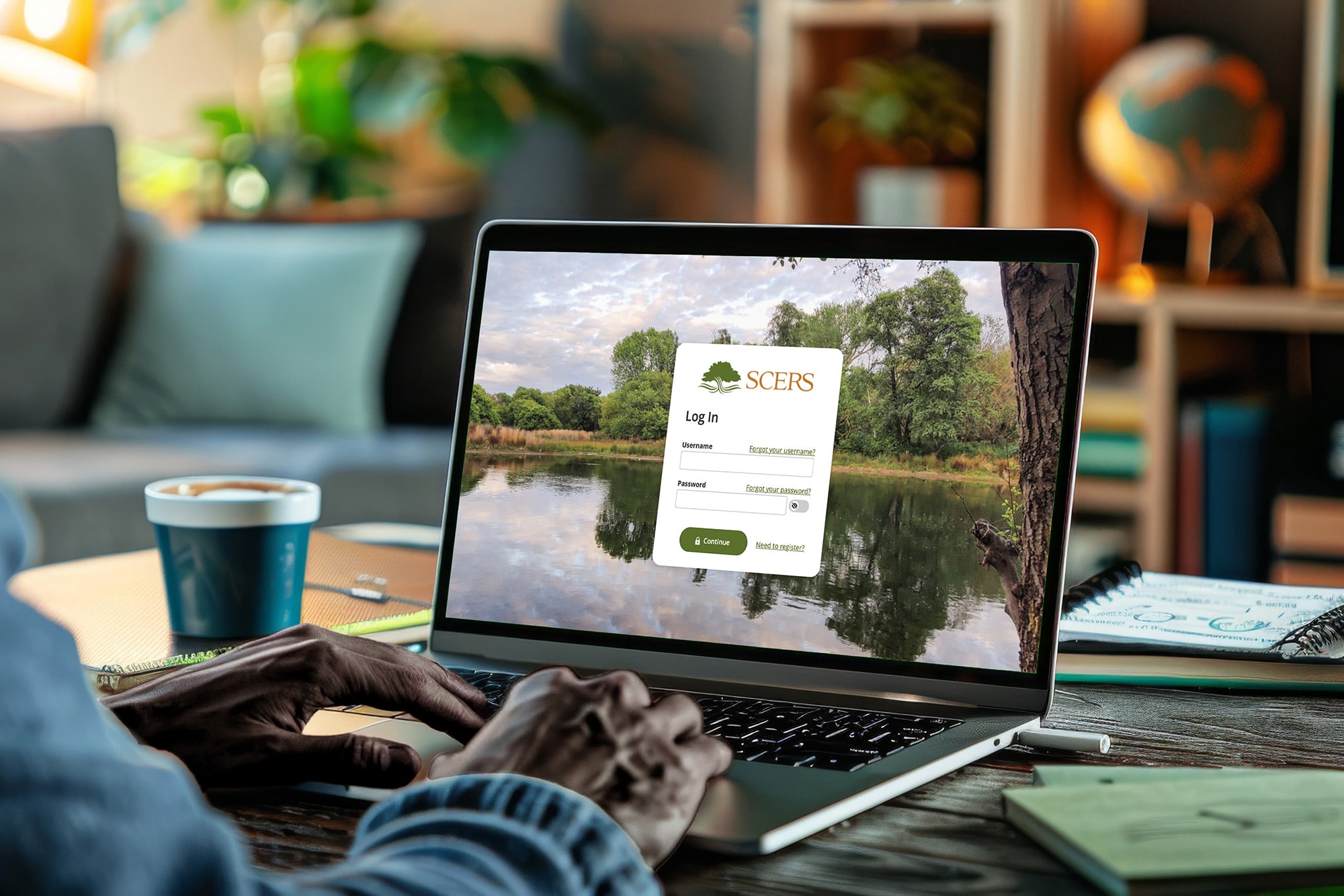 A person types on a laptop displaying a serene lakeside scene with a login screen. A cozy home office surrounds them, featuring a globe and a coffee cup.